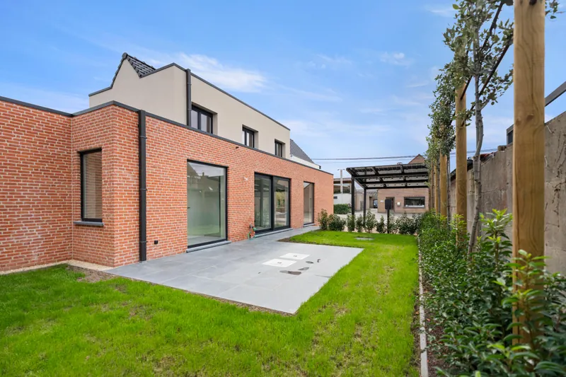 Achtergevel en tuin van de gerenoveerde woning in Torhout met zicht op de carport achteraan